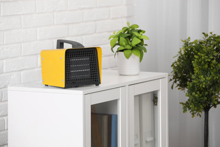 Modern electric fan heater near notebooks and houseplant on white table in room