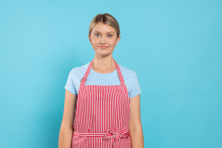 Beautiful young woman in clean striped apron on light blue backgroundの写真素材