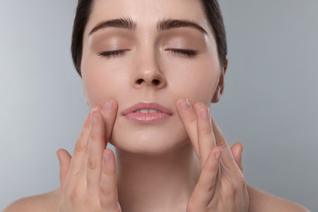 Young woman massaging her face on gray backgroundの写真素材