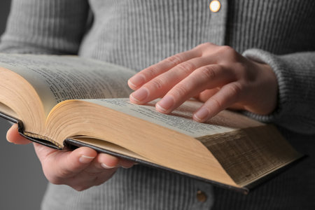 Woman reading Bible against gray background, closeup