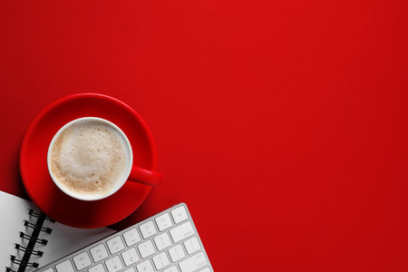 Cup with aromatic cappuccino, notepad and keyboard on red background, flat lay. Space for textの写真素材