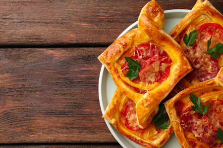 Fresh delicious puff pastry with cheese, tomatoes and parsley on wooden table, top view. Space for textの写真素材