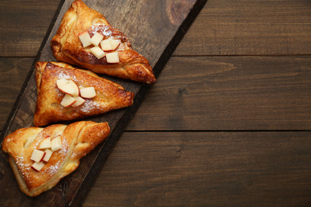 Fresh tasty puff pastry with sugar powder and apples served on wooden table, top view. Space for textの写真素材