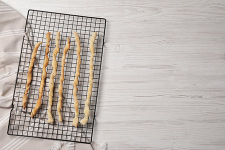 Rack with homemade breadsticks on white wooden table, top view and space for text. Cooking...