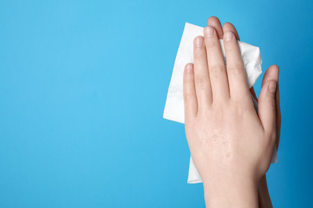 Woman wiping hands with paper towel on light blue background, closeup. Space for textの写真素材