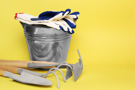 Bucket with gardening gloves and tools on yellow background. Space for textの写真素材