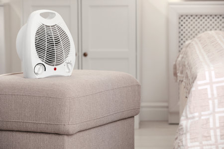 Modern electric fan heater on pouf in cozy roomの写真素材