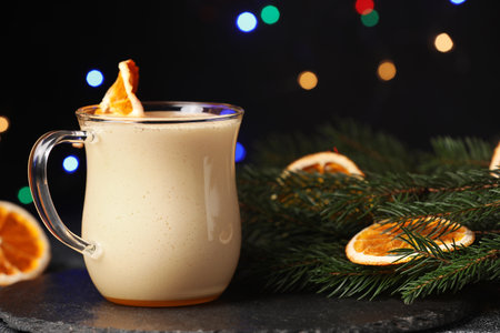 Glass cup of delicious eggnog with dried orange slice and fir branch on black tableの写真素材