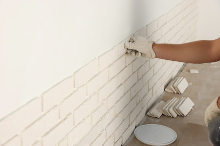 Worker installing decorative wall tiles in room, closeup
