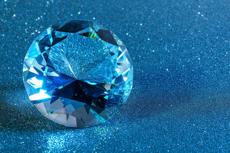 Beautiful dazzling diamond on light blue glitter background, closeup. Space for textの写真素材