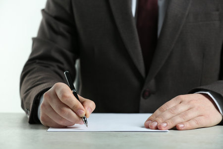 Man writing on sheet of paper with pen at white table, closeupの写真素材