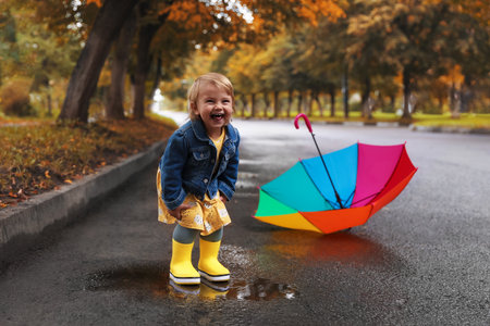 Cute little girl standing in puddle near colorful umbrella outdoorsの写真素材