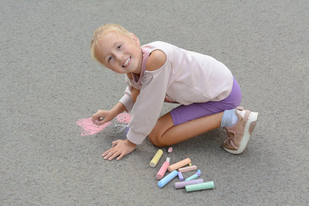 Little child drawing butterfly and heart with chalk on asphaltの写真素材