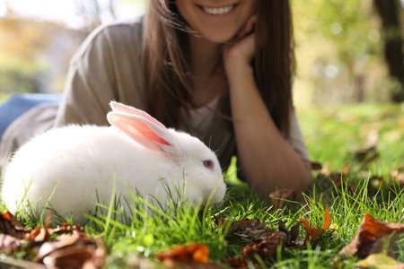 Happy woman with cute white rabbit on grass in park, closeupの写真素材