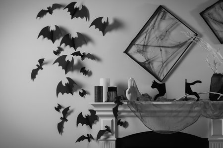 Black frames with cobweb on white wall, paper bats and different Halloween decor on fireplace...