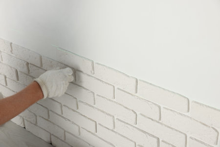 Worker installing decorative wall tiles in room, closeupの写真素材