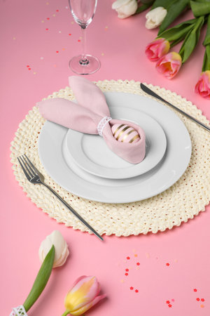 Festive table setting with painted egg, plates and tulips on pink background. easter celebration