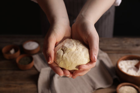 Woman with fresh dough on wooden table with ingredients, closeup. Cooking traditional grissiniの写真素材