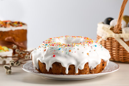Delicious Easter cake decorated with sprinkles near painted eggs and willow branches on white wooden...