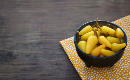 Bowl of pickled yellow jalapeno peppers on wooden table. Space for textの写真素材