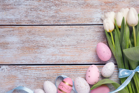 Many painted Easter eggs, tulip flowers and ribbon on rustic wooden table, flat lay. Space for text
