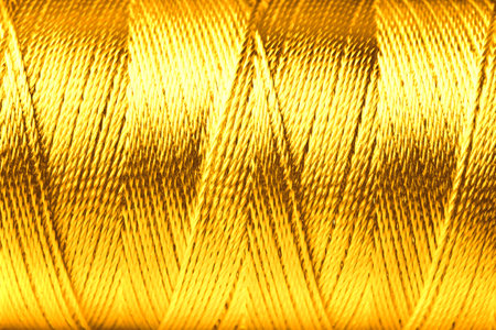Spool of golden sewing thread as background, closeupの写真素材