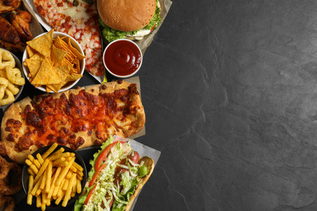 Burger, pizza and other fast food on black table, flat lay with space for textの写真素材