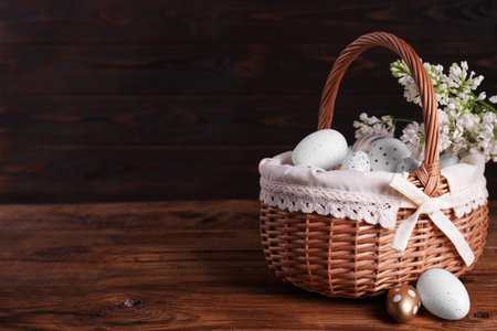 Wicker basket with festively decorated Easter eggs and white lilac flowers on wooden table. Space for textの写真素材