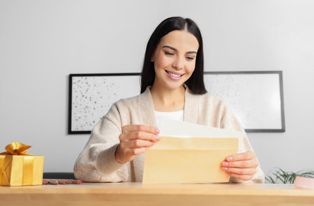 Happy woman reading greeting card at wooden table in roomの写真素材