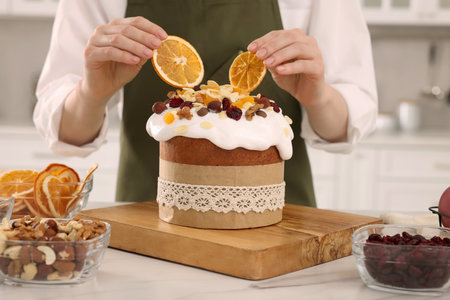 Woman decorating traditional Easter cake with dried orange slices at white marble table in kitchen,...