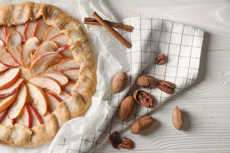 Delicious apple galette, cinnamon and pecans on white wooden table, flat layの写真素材