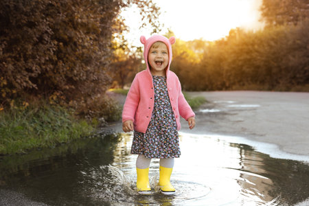 Little girl wearing rubber boots walking in puddle outdoorsの写真素材