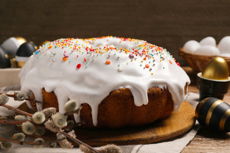 Delicious Easter cake decorated with sprinkles near eggs and willow branches on wooden table,...