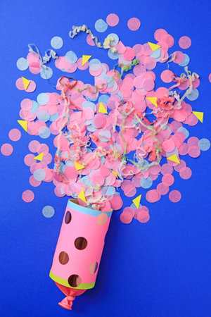 Colorful confetti and streamers bursting out of party cracker on blue background, flat layの写真素材