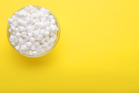 Glass bowl with delicious marshmallows on yellow background, top view. Space for textの写真素材
