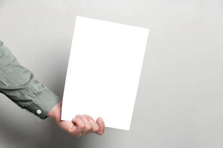 Man holding sheet of paper on gray background, closeup. Mockup for designの写真素材