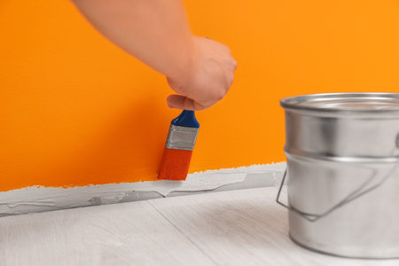 Worker using brush to paint wall with orange dye indoors, closeupの写真素材