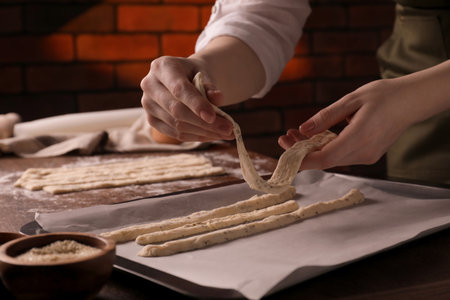Woman homemade breadsticks on baking sheet at wooden table indoors, closeup. Cooking traditional grissiniの写真素材