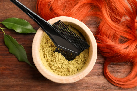 Bowl of henna powder, brush, green leaves and red strand on wooden table, flat lay. natural hair coloringの写真素材