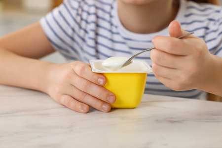 Cute little girl with tasty yogurt at white marble table, closeupの写真素材