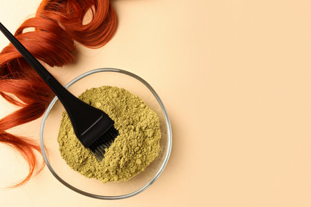 Bowl of henna powder, brush and red strand on beige background, flat lay with space for text. Natural hair coloringの写真素材