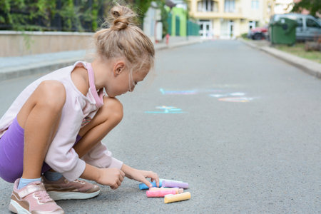 Little child with chalk pieces sitting on asphalt outdoors, space for textの写真素材