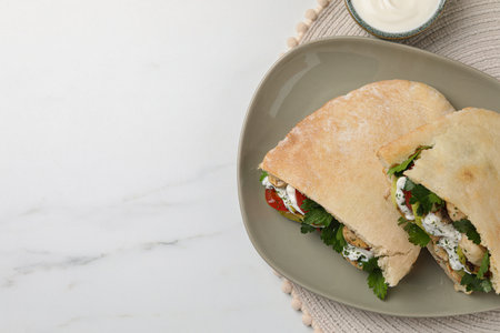Delicious pita sandwiches with grilled vegetables and sour cream sauce on white marble table, flat...