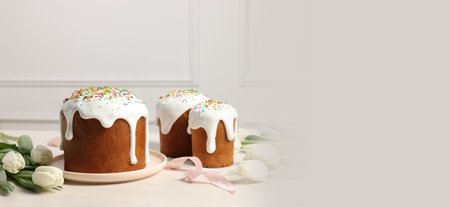 Delicious Easter cakes with sprinkles and beautiful tulips on white wooden table, space for text....