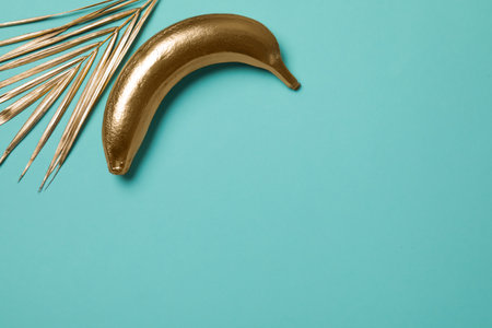 Golden banana and palm leaf on turquoise background, top view. Space for textの写真素材