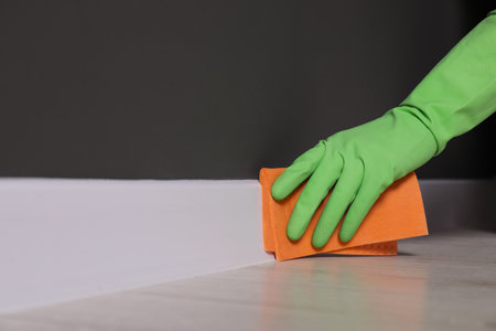 Woman in protective glove cleaning plinth with sponge cloth indoors, closeup. Space for textの写真素材