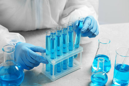 Scientist taking test tube with light blue liquid at white table in laboratory, closeupの写真素材