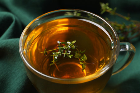 Glass cup of aromatic herbal tea with thyme on green fabric, closeupの写真素材