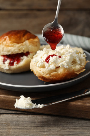 Pouring cranberry jam from spoon into freshly baked soda water scone on wooden tableの写真素材