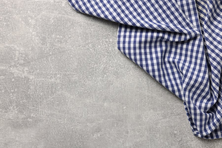 Blue checkered tablecloth on light gray textured table, top view. Space for text